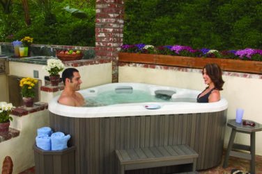 Couple inside of hot tub on patio with outdoor furniture and grill